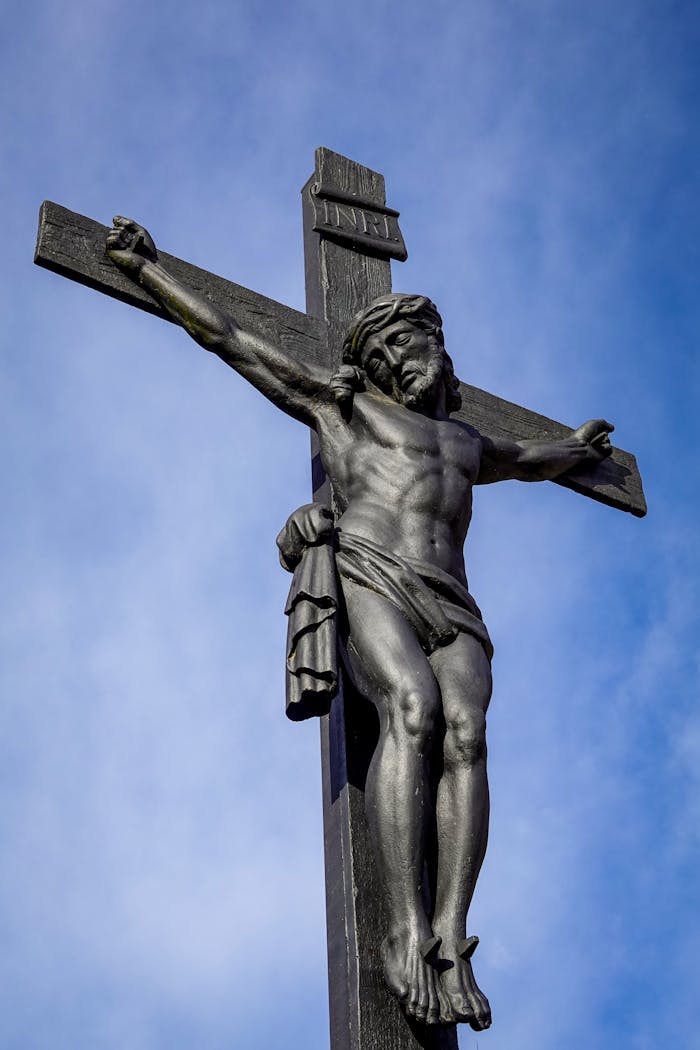 High-angle view of a crucifix statue of Jesus against a clear blue sky, symbolizing Christianity.
